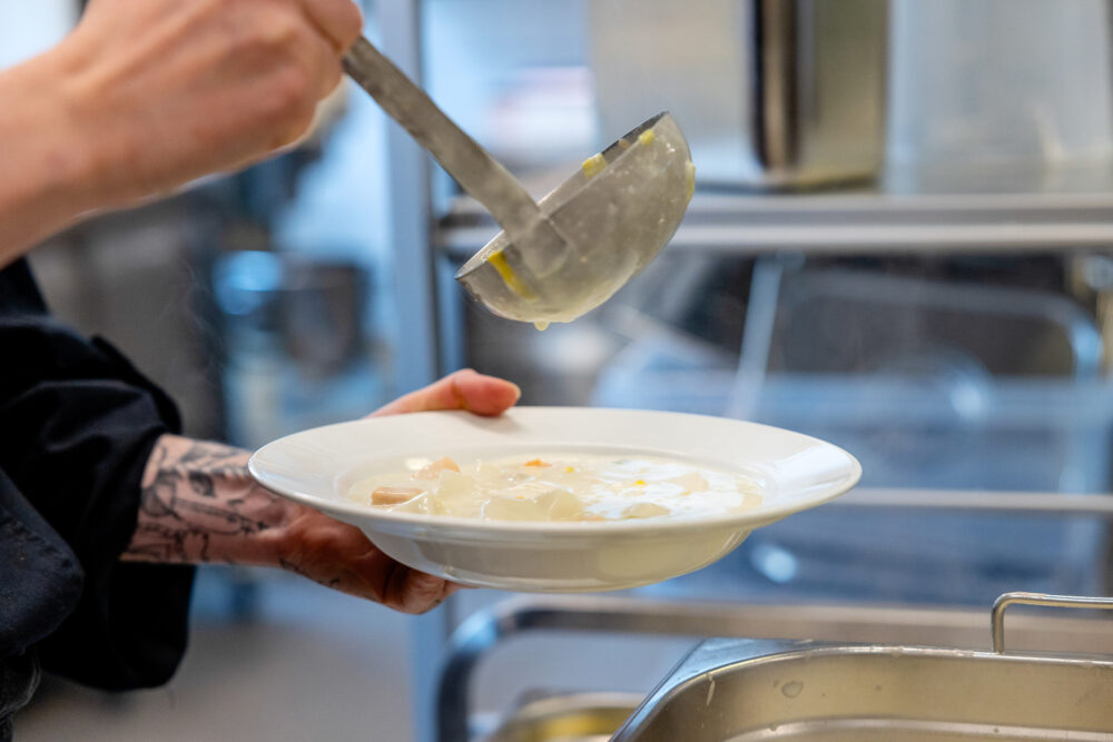 En hånd som øser suppe opp i en tallerken.