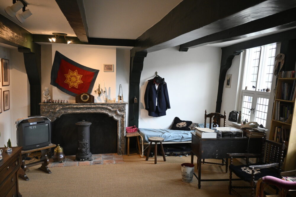 Et rom med seng, TV, peis, skrivebord og kommode. Frelsesarmeens banner henger på veggen sammen med en mørk uniform og bonnett.