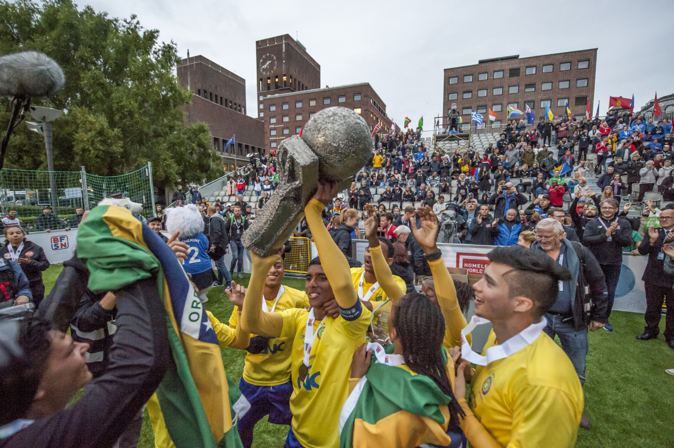 Foto: Players in yellow soccer jerseys cheering after a match. One man is holding up the big prize.
