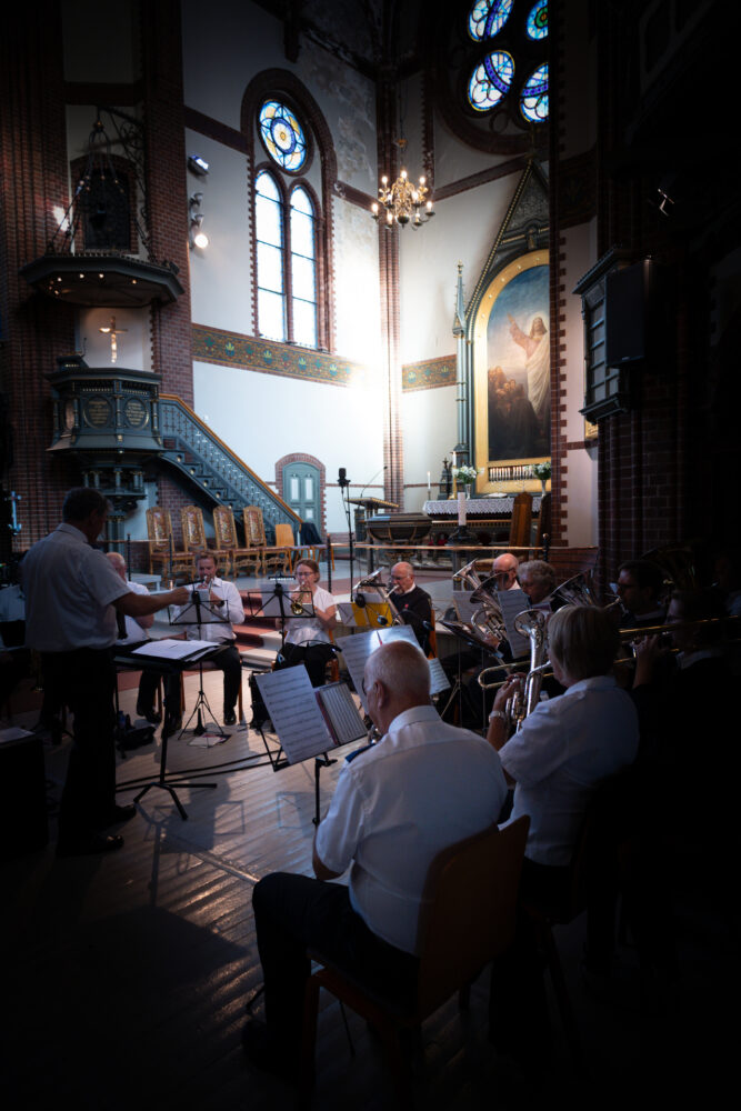 Foto: Kirkerom med folk som sitter i salen. Flere av vinduene har glassmalerier.